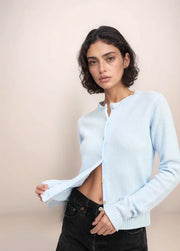 Woman wearing a light blue sweater over a white top with black jeans on a beige background