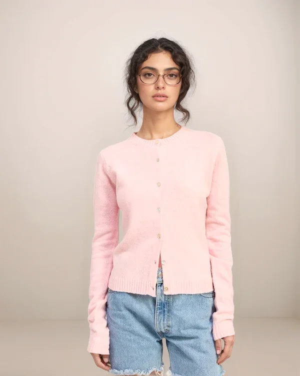 Woman wearing a pink cardigan and blue jeans against a plain background