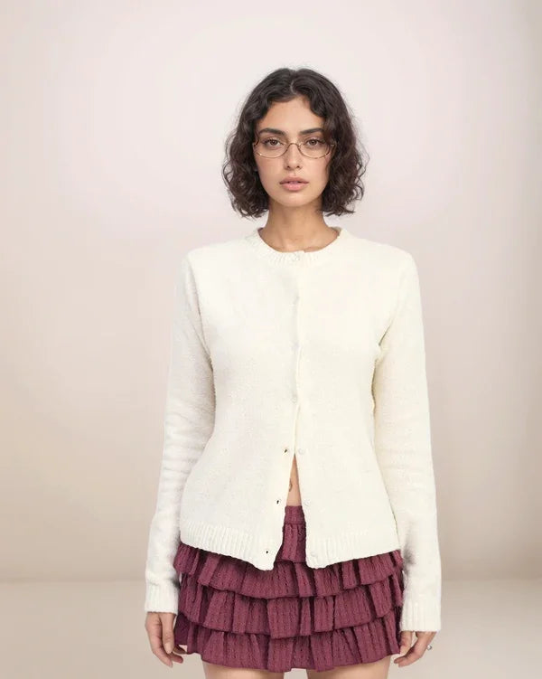 Woman wearing a white cardigan over a maroon skirt on a plain background