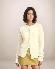 Woman wearing a light-colored cardigan and green skirt against a plain background