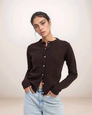 Woman wearing a brown cardigan over a black top with light blue jeans on a plain background