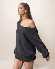 Woman wearing a dark gray off-shoulder sweater against a plain background