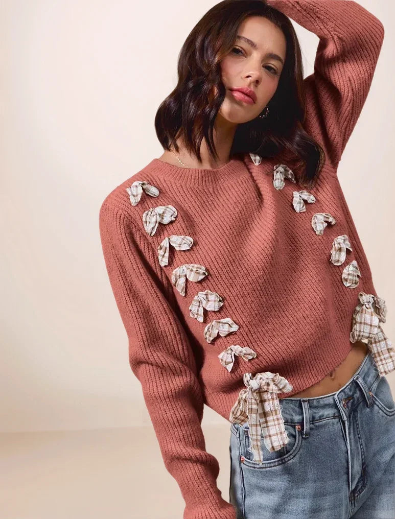 Woman wearing a rust color sweater with decorative elements on a plain background