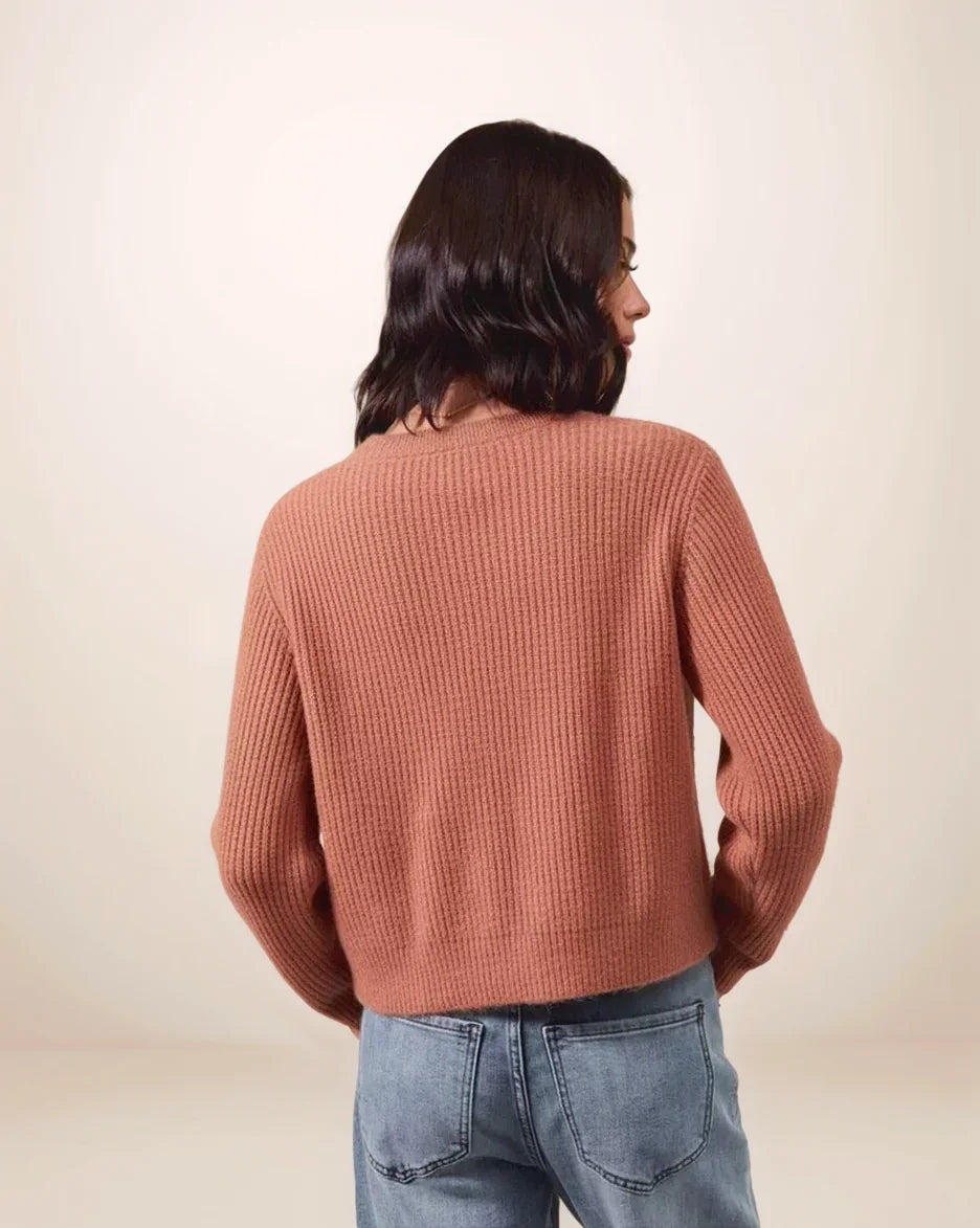 Person wearing a rust colored ribbed sweater and blue jeans on a beige background