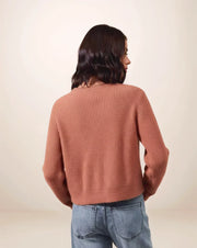 Person wearing a rust colored ribbed sweater and blue jeans on a beige background