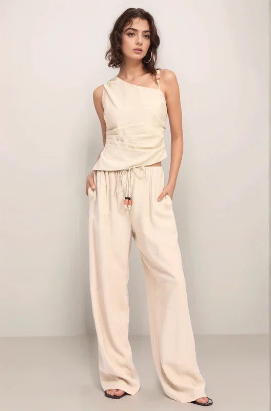 Full-body shot of a model wearing the complete Sonora set, featuring the asymmetrical embellished top and matching wide-leg pants in a monochromatic natural hue.
