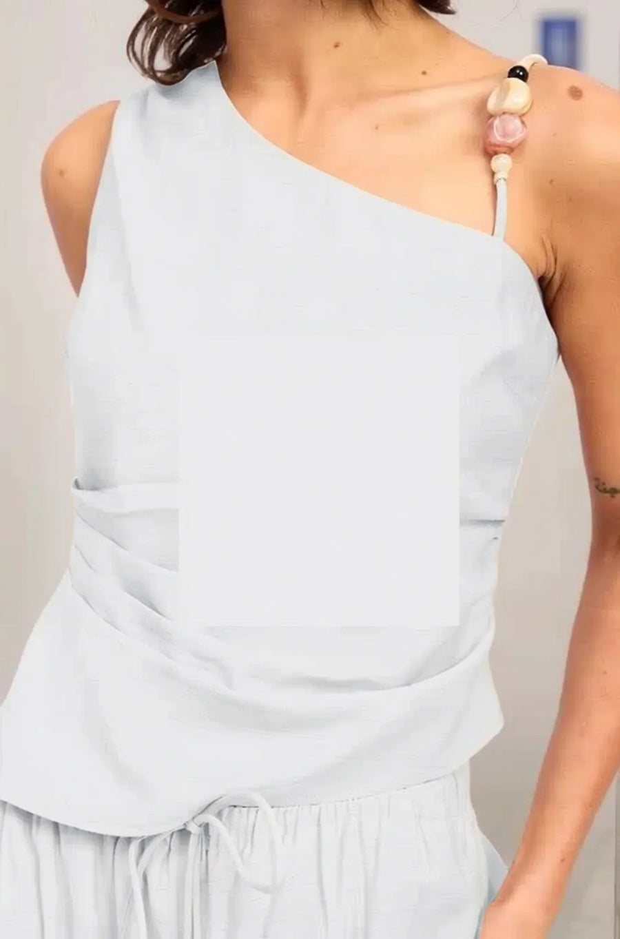 A detailed close-up of the white Sonora top's shoulder strap, highlighting the oversized artisanal beads and earth-toned stone embellishments.