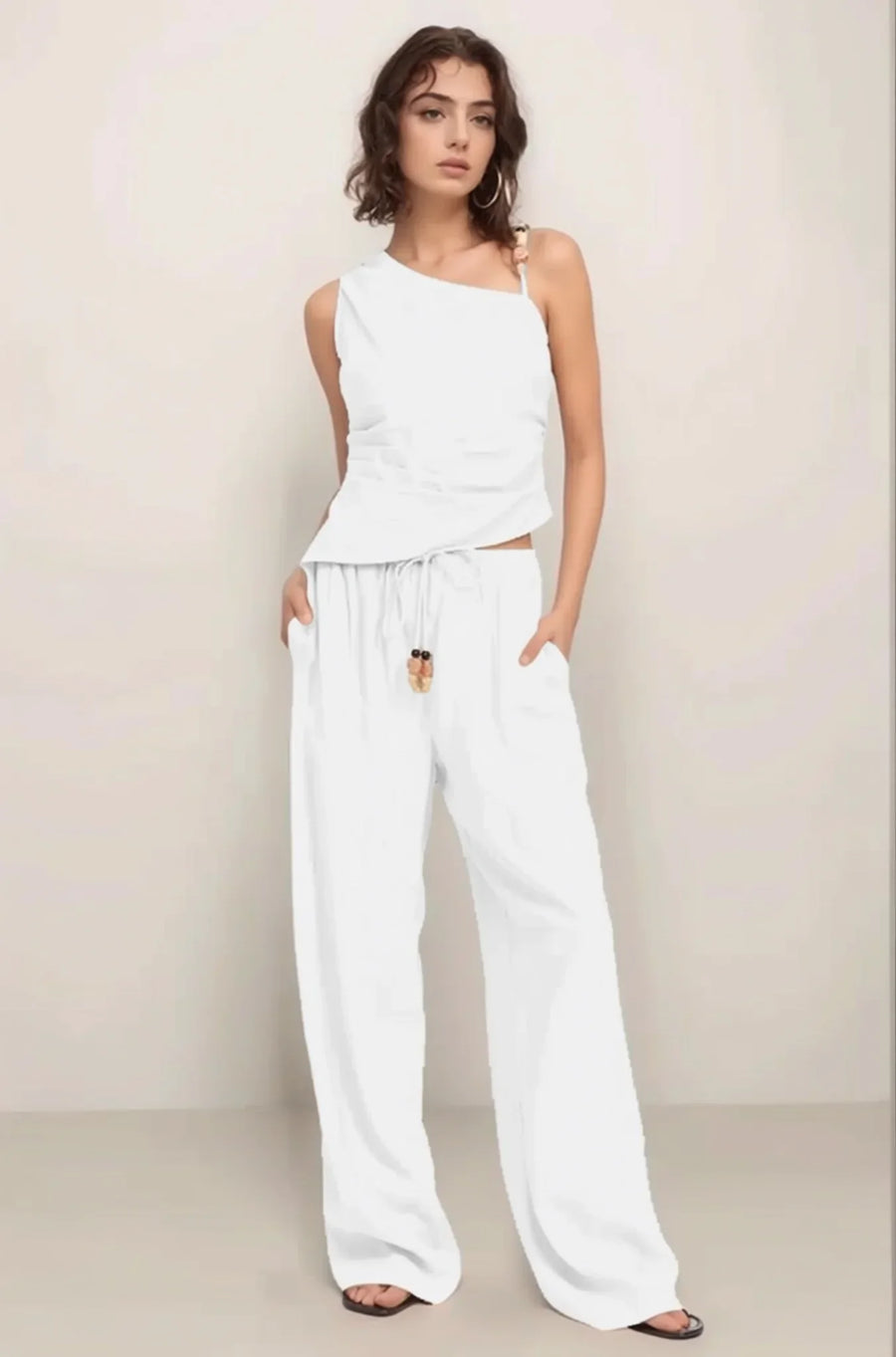 Full-body shot of a model wearing the complete Sonora set in white, featuring the asymmetrical embellished top and matching wide-leg pant.