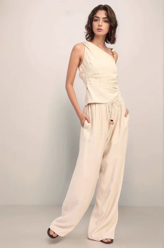 Front view of a model wearing the complete Sonora set, featuring the asymmetrical one-shoulder top and baggy wide-leg pants in a monochromatic sand hue.