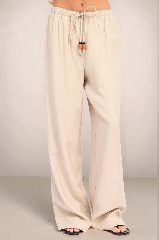 Close-up front view of the sand-colored Sonora pants, highlighting the low-rise elastic waistband and the functional drawstring tie embellished with oversized multi-tonal beads.