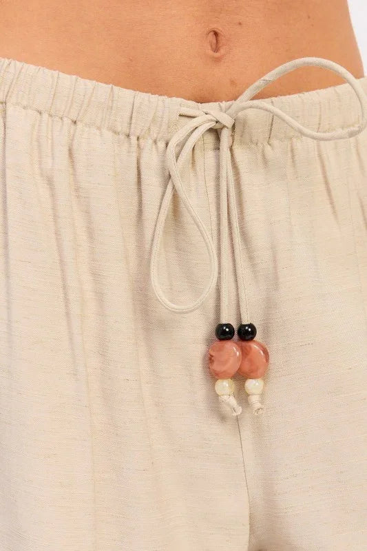 A macro close-up of the Sonora pants' drawstring hardware, emphasizing the hand-crafted detail of the earth-toned stone and resin beads.