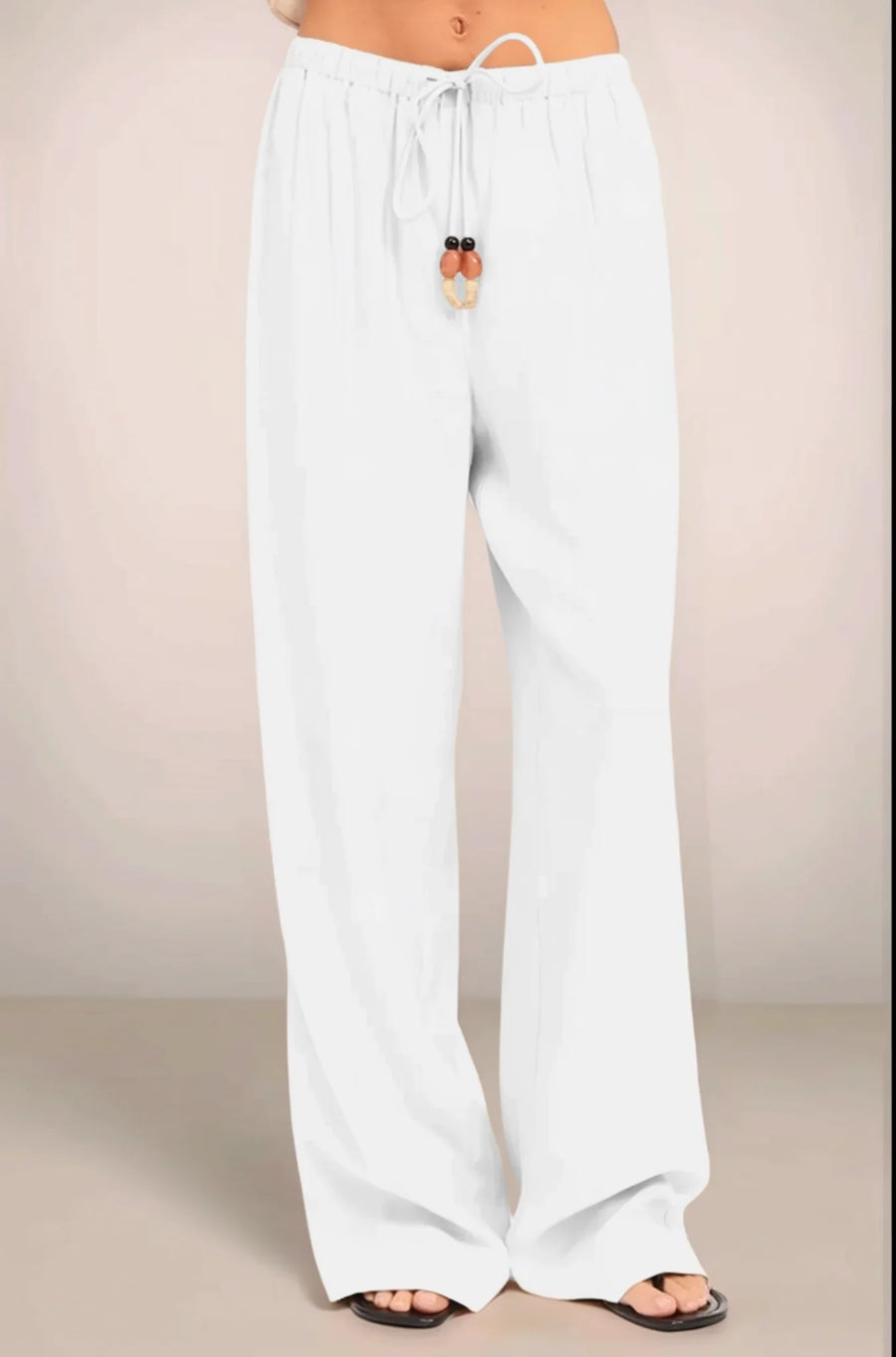 Close-up front view of the white Sonora pants, highlighting the low-rise elastic waistband and the functional drawstring tie embellished with oversized multi-tonal beads.