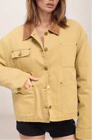 Person wearing a mustard yellow jacket with brown collar on a plain background