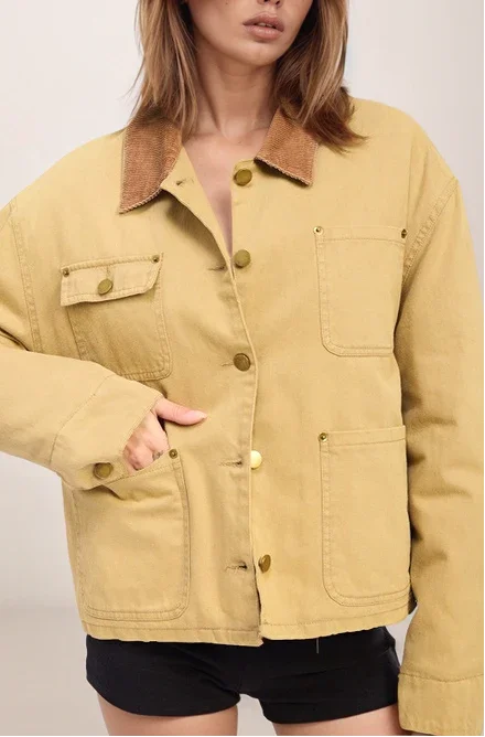 Person wearing a mustard yellow jacket with brown collar on a plain background