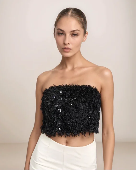 Model wearing a black sequin strapless top and white pants against a neutral background