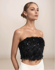 Woman wearing a black strapless top with sequins on a beige background