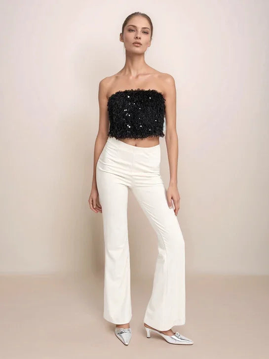 Model wearing a black sequin top and white pants against a beige background