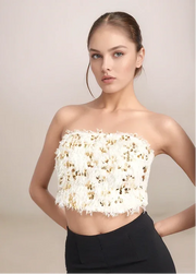 Woman wearing a white strapless top with gold embellishments against a beige background