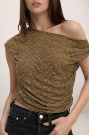 Woman wearing a gold off-shoulder top with black pants on a plain background