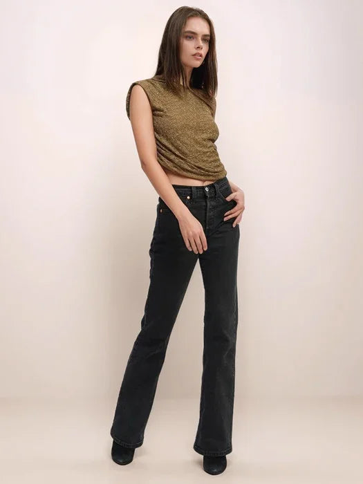 Woman wearing a green sleeveless top and black jeans against a white background