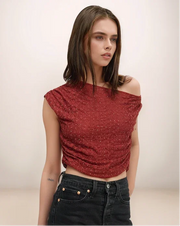Woman wearing a red off-shoulder top and black jeans against a plain background