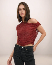 Woman wearing a red off-shoulder top and black jeans against a plain background