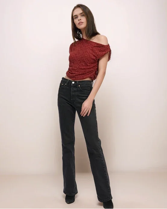 Woman wearing a red off-shoulder top and black jeans against a plain background
