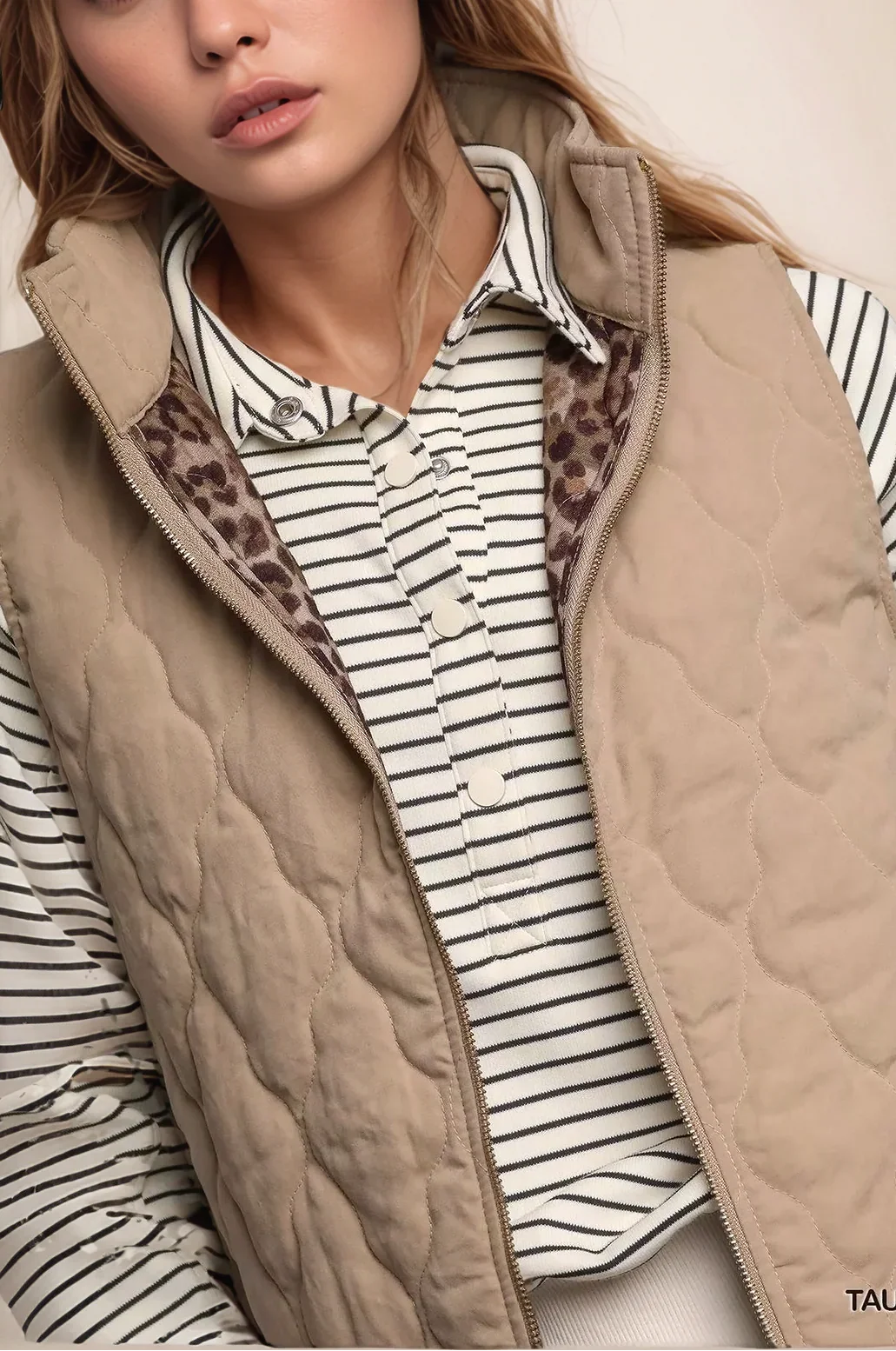 Person wearing a beige quilted vest over a striped shirt with leopard print lining.