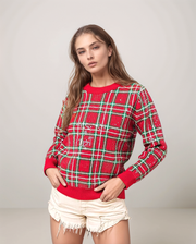 Woman wearing a red and green plaid sweater with white shorts on a gray background
