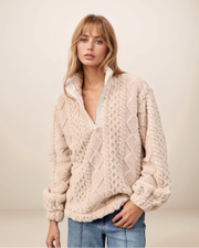 Woman wearing a beige cable knit sweater against a plain background