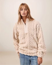 Woman wearing a cream knitted sweater and blue jeans against a plain background