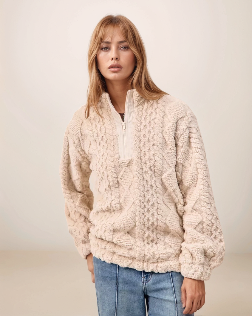 Woman wearing a cream knitted sweater and blue jeans against a plain background