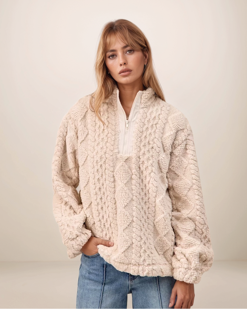 Woman wearing a cream cable knit sweater against a plain background