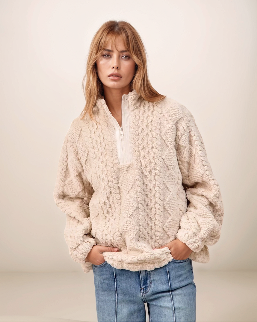 Woman wearing a cream cable knit sweater and blue jeans against a plain background