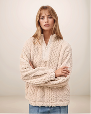 Woman wearing a beige cable knit sweater against a plain background