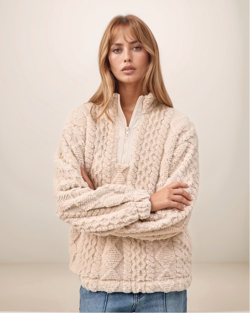 Woman wearing a beige cable knit sweater against a plain background