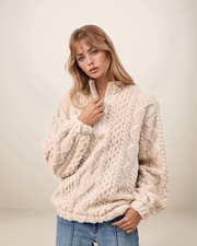 Woman wearing a beige cable knit sweater against a plain background