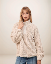 Woman wearing a cream knitted sweater against a plain background
