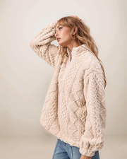 Woman wearing a cream sherpa jacket against a plain background