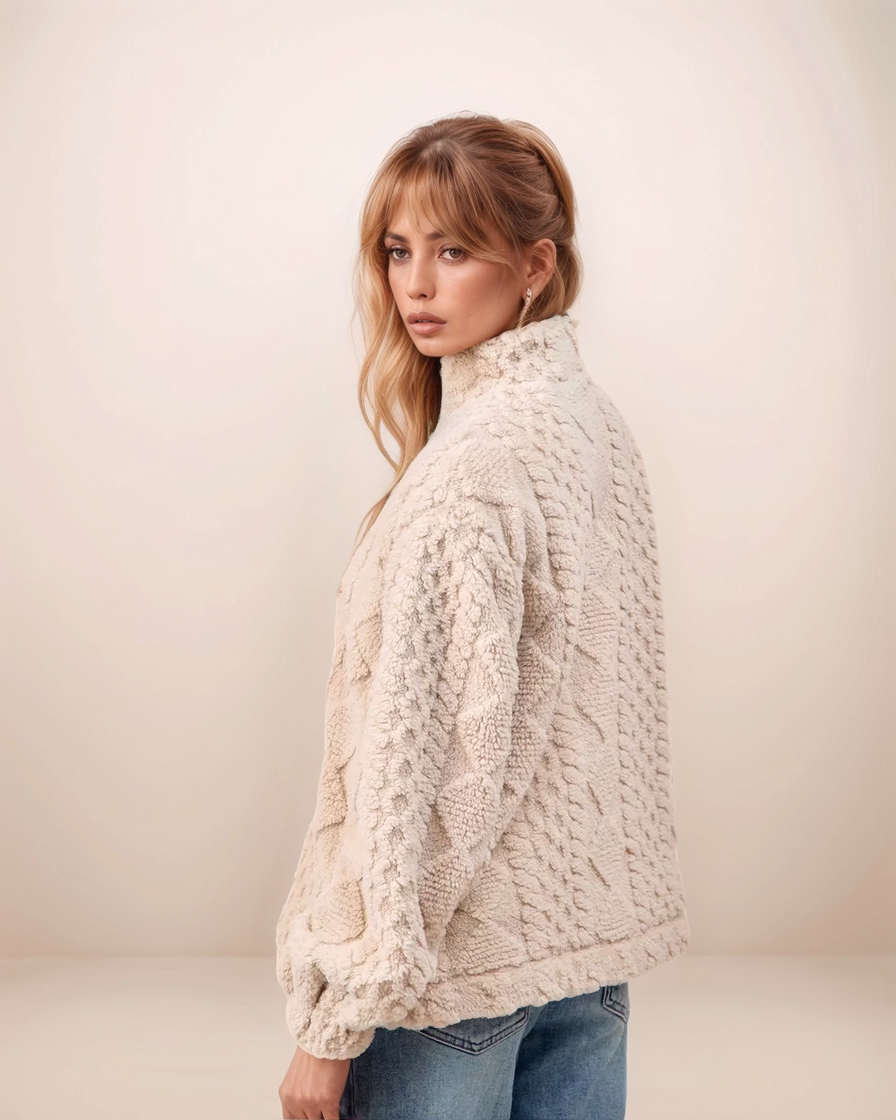 Woman wearing a cream knitted sweater against a plain background