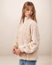 Woman wearing a cream chunky knit sweater against a plain background