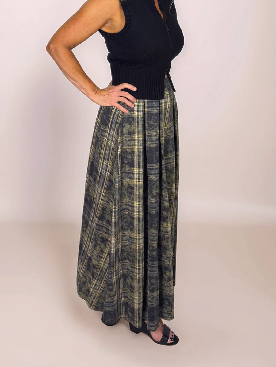 Woman wearing a black top and plaid skirt against a plain background