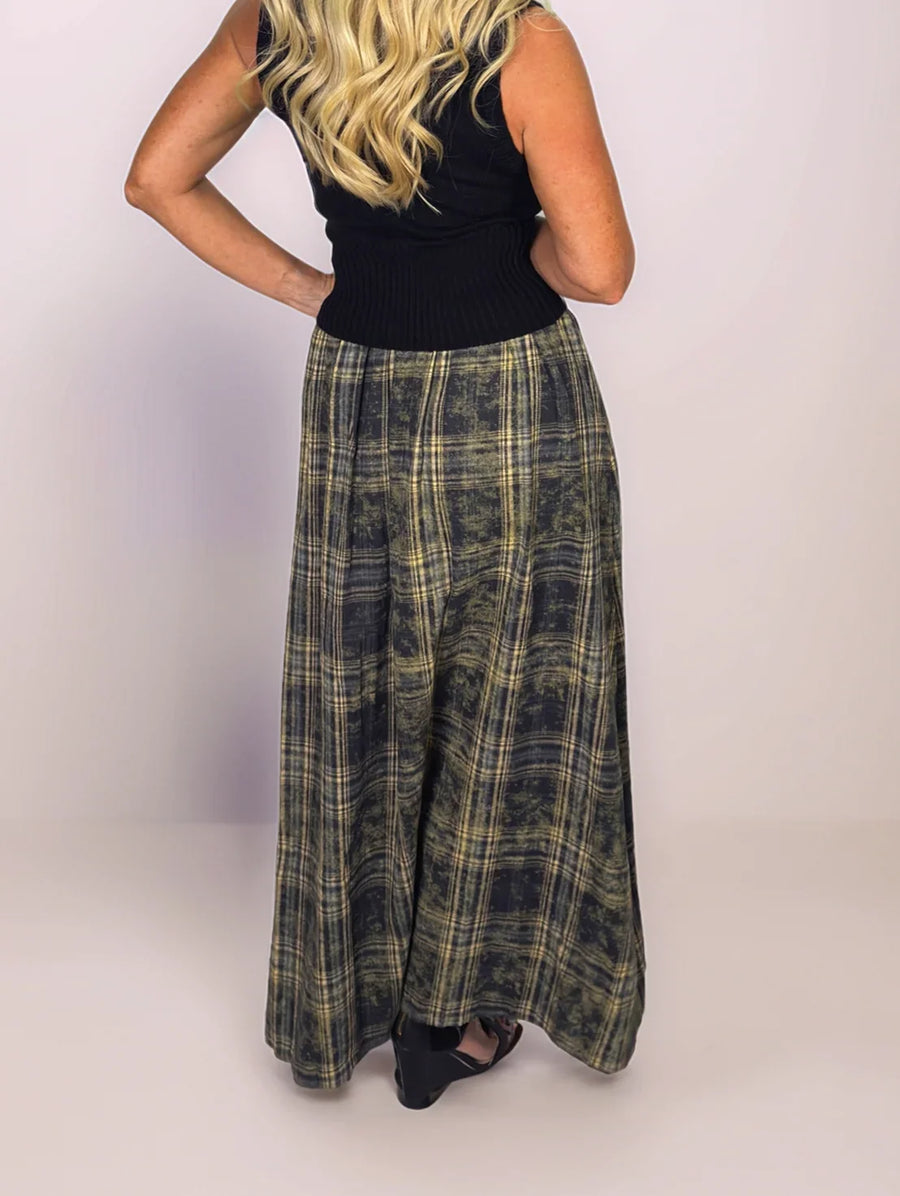 Person wearing a black top and plaid skirt on a plain background