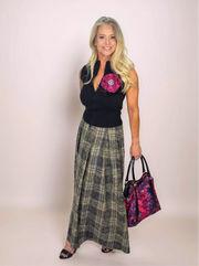 Woman wearing a black sleeveless top with a pink flower and a plaid skirt, holding a matching handbag.