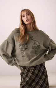 Woman wearing a green sweater with rooster design on a plain background
