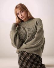 Woman wearing a gray sweater with a tiger design on a plain background