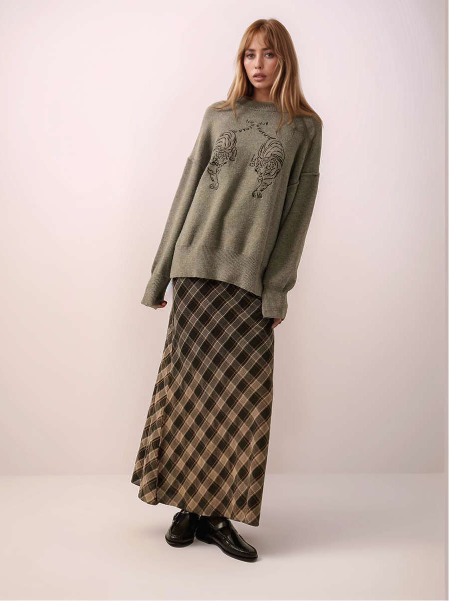 Woman wearing a gray sweater with a graphic design and a plaid skirt on a white background