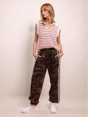 Woman wearing a striped sleeveless top and camouflage pants with white stripes on a plain background