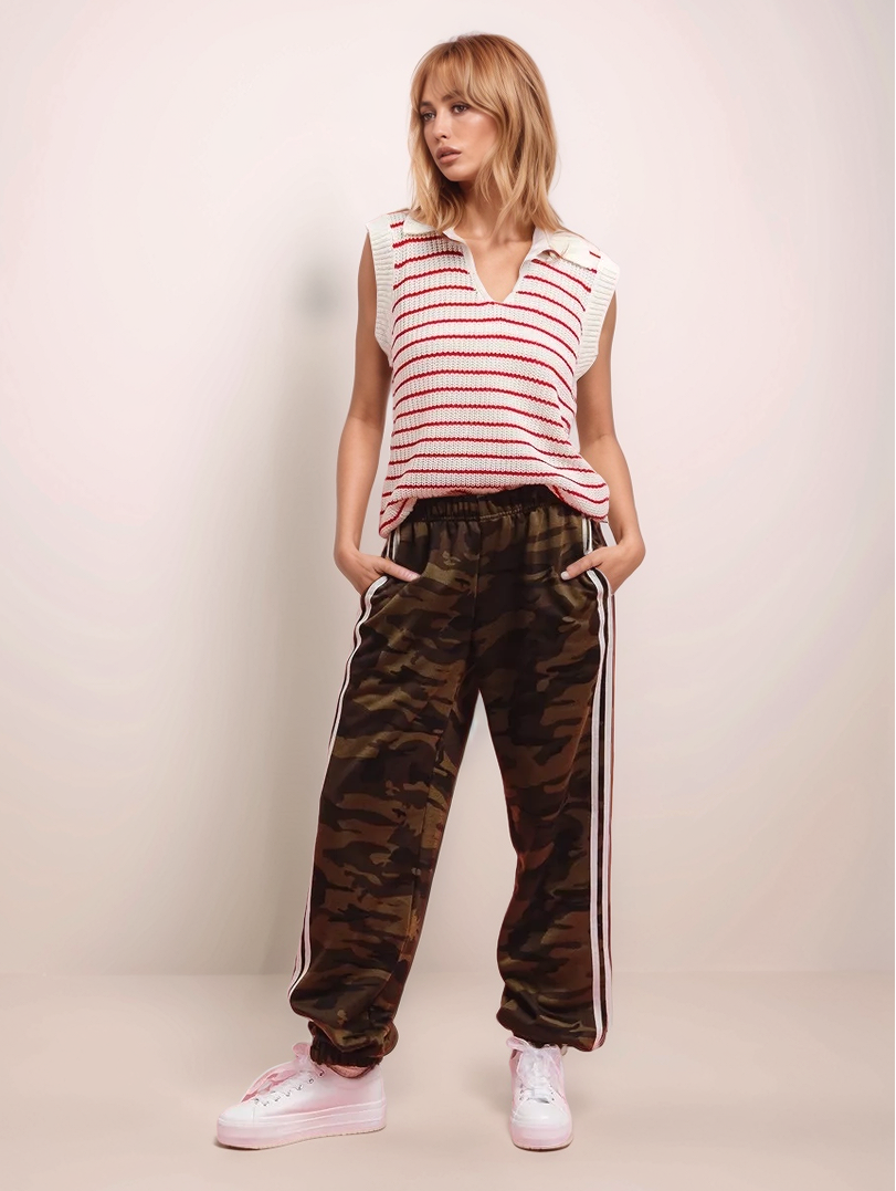 Woman wearing a striped sleeveless top and camouflage pants with white stripes on a plain background