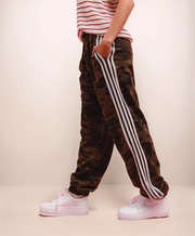 Camouflage jogger pants with white stripes worn by a person on a plain background